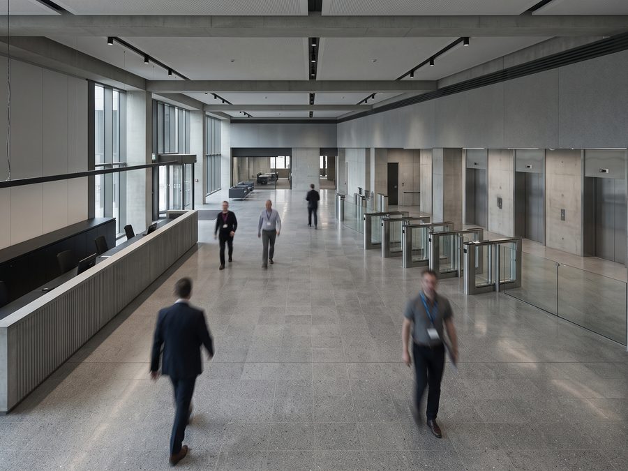 An institutional building lobby seen from above, speed gates and lift banks beyond.