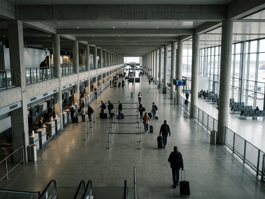 An airport terminal concourse seen from above, travellers crossing a long hall.
